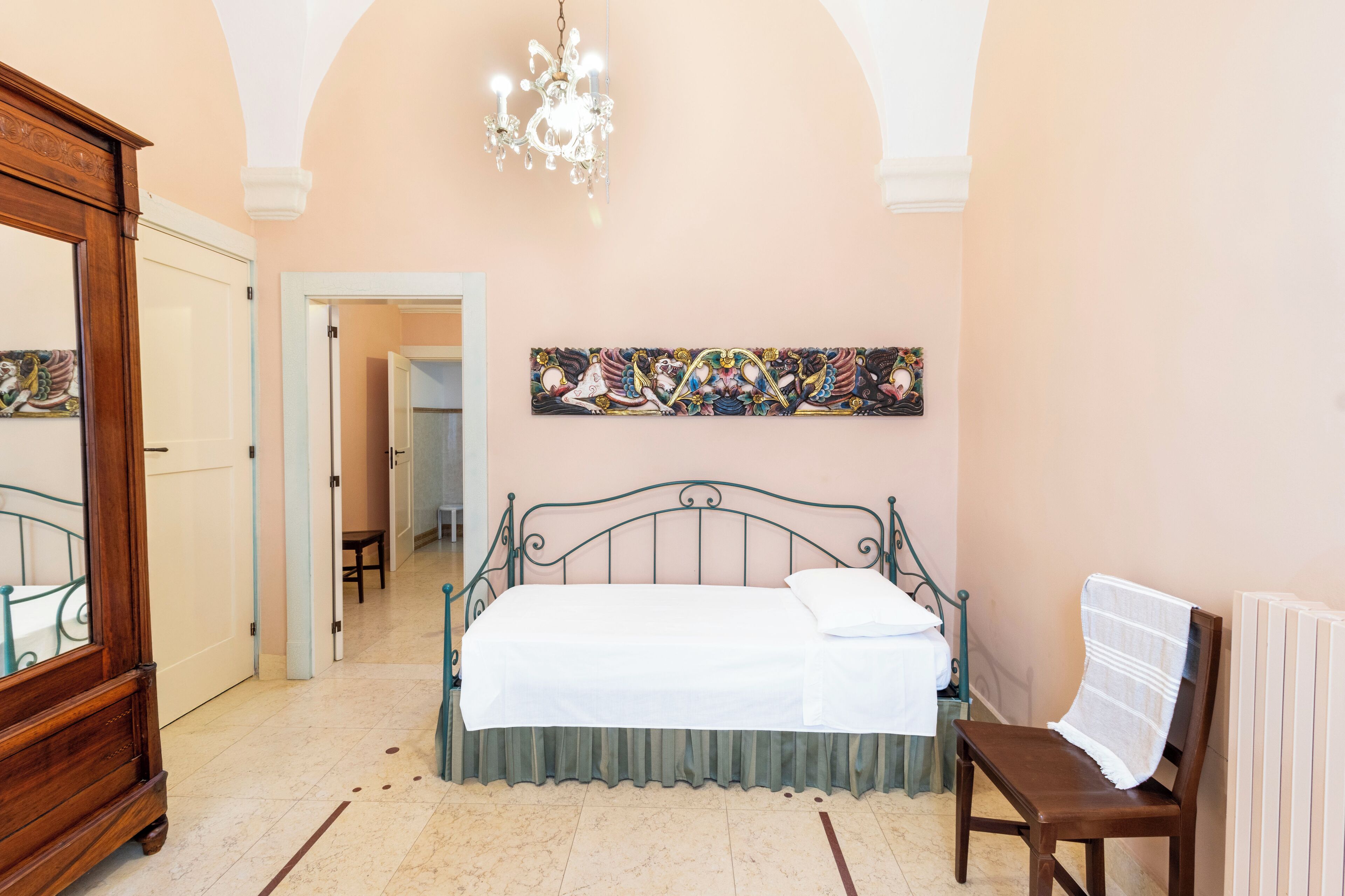 A bedroom with a bed, a chair, a dresser, and a chandelier.