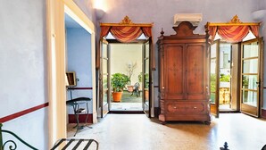 A hallway with a wooden cabinet, a bench, and a door leading to an outdoor area with potted plants. - Palazzo Insula (Gallipoli)