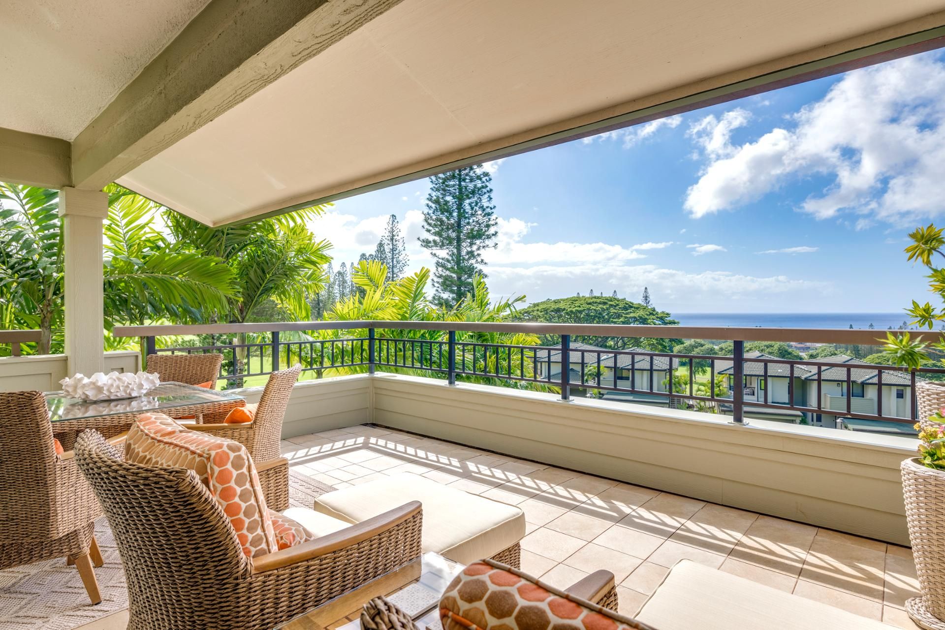 A covered outdoor seating area with wicker furniture, a view of the ocean, and lush greenery.