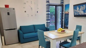 Una cocina moderna con un refrigerador empotrado, un sofá azul, una mesa de comedor con sillas y un frutero.