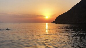 Un atardecer sobre aguas tranquilas con barcos y un acantilado.