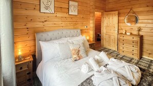 A wooden cabin bedroom with a bed, nightstands, a dresser, and artwork on the walls. - 3 bedroom accommodation in Falkirk (Falkirk)