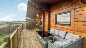A wooden deck with a wicker sofa and table, a view of the countryside, and a wooden fence. - 3 bedroom accommodation in Falkirk (Falkirk)
