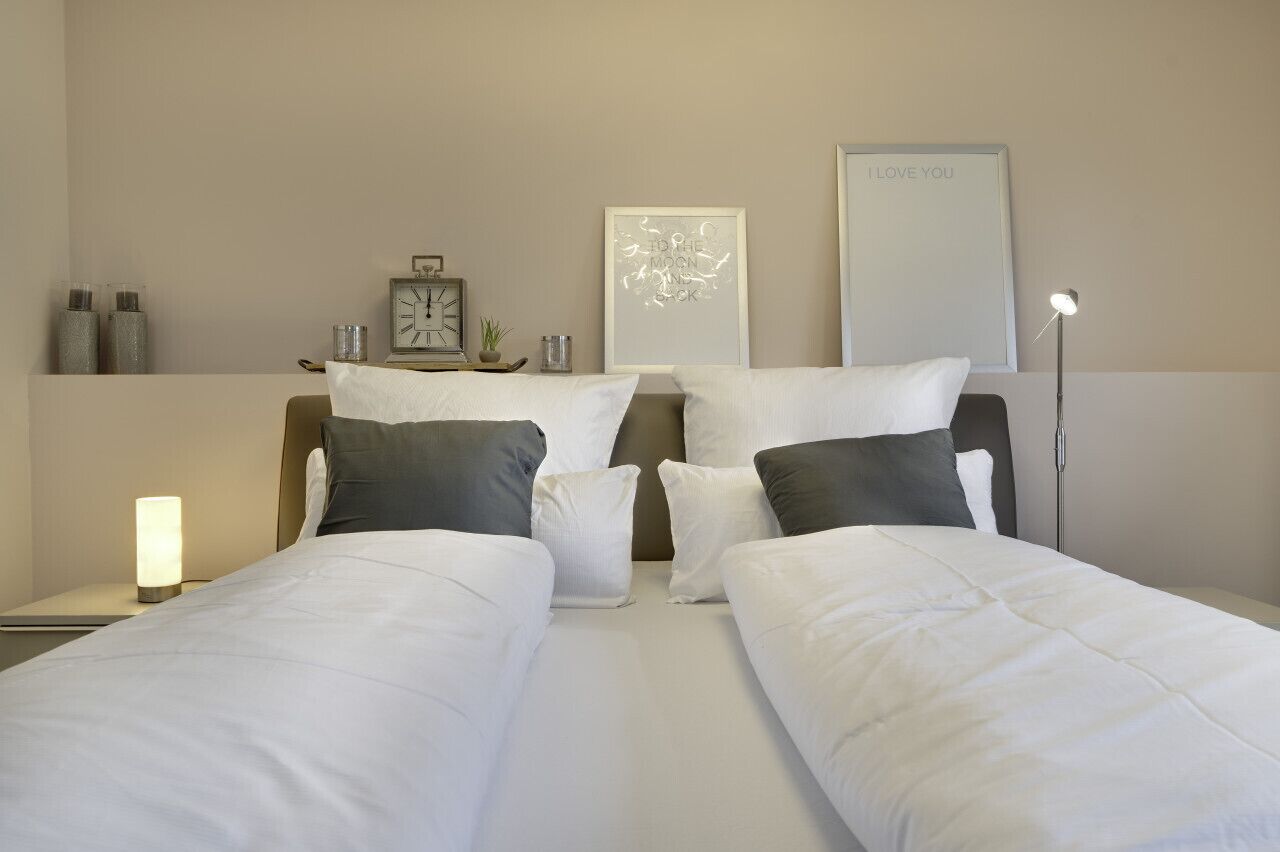 Een hotelkamer met twee bedden, een nachtkastje met een lamp, een klok, decoratieve objecten en een lijst aan de muur.