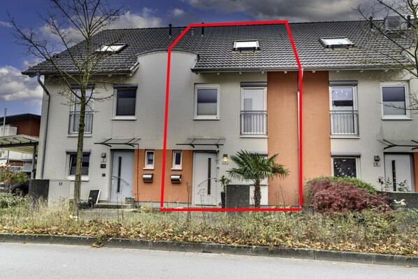 A two-story residential building with a grey facade, multiple windows, and a red outline marking a section.