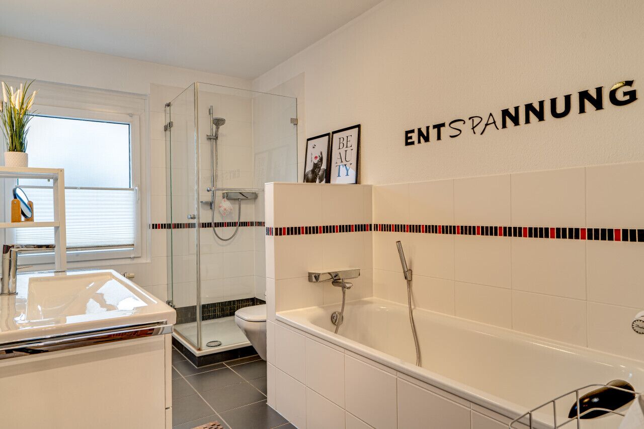 A modern bathroom with a glass shower enclosure, a bathtub, and a toilet. There is a shelf with a plant and a towel rack.