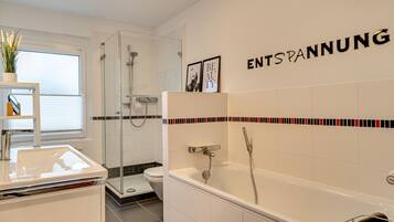 A modern bathroom with a glass shower enclosure, a bathtub, and a toilet. There is a shelf with a plant and a towel rack.