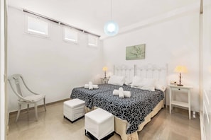 Een slaapkamer met twee bedden, een stoel, een nachtkastje en een lamp.