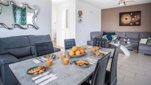 A modern living room with a grey sofa, a dining table set with breakfast, and a ceiling fan.