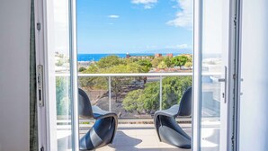 A balcony with two chairs and a view of the sea and buildings.