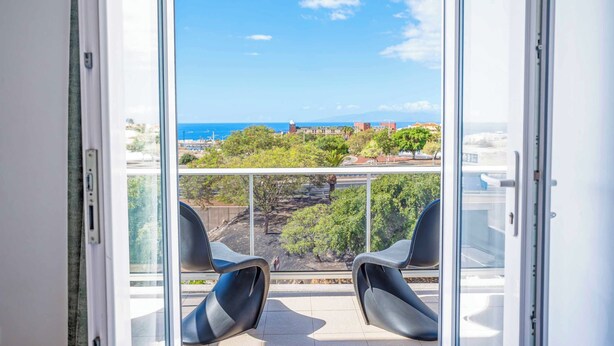 A balcony with two chairs and a view of the sea and buildings.