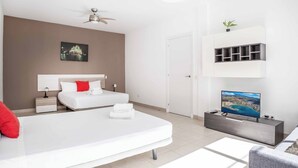 A modern hotel room with a bed, a TV, a bedside table, a nightstand, a ceiling fan, a wall-mounted shelf with a plant, and a framed picture on the wall.