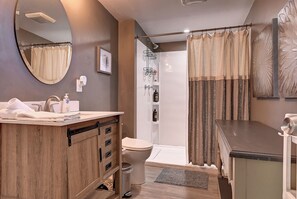 Un baño moderno con tocador de madera, inodoro, ducha con puerta de vidrio y un espejo grande.