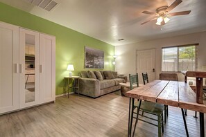 A room with a green wall, a wooden dining table, a sofa, a ceiling fan, and a window with blinds. - Designer Condo in Hip Zen Yard! Midtown Phoenix! (Phoenix)