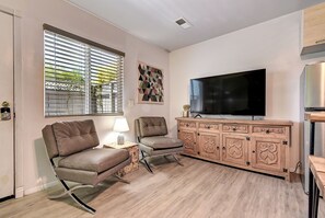 A living room with a TV, two chairs, a wooden cabinet, and a window with blinds.