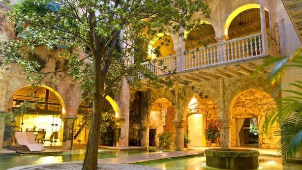 An indoor courtyard with a pool, stone arches, and a tree. - Casa Pombo 102 (Cartagena)