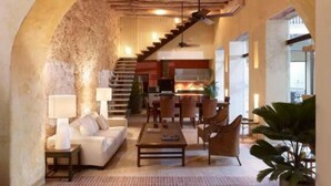 A spacious living area with a high ceiling, a staircase leading to an upper level, and a large archway. - Casa Pombo 102 (Cartagena)