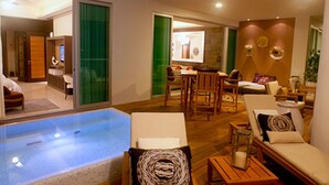 Quarto de hotel moderno com piscina envidraçada, área de refeições e sala de estar com sofá e poltronas.
