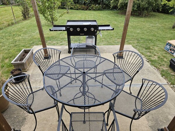 Eine Terrasse mit einem runden Metalltisch, vier Stühlen, einem Grill und einem kleinen Blumentopf.