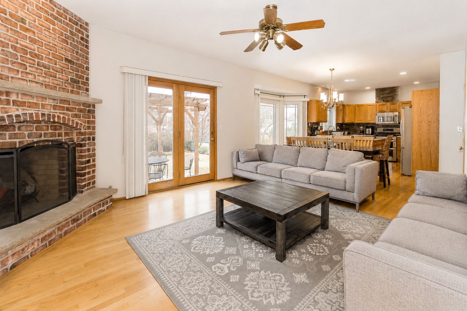 A living room with a fireplace, a sofa, a coffee table, and a kitchen in the background.