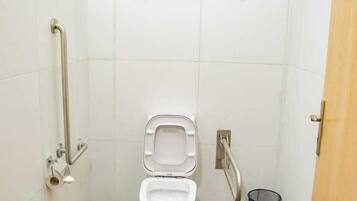 Un baño pequeño con azulejos, que incluye inodoro, barras de apoyo, ventana y cubo de basura.