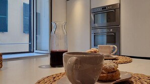 Una cocina moderna con horno empotrado, una mesa de centro con una taza y pasteles, y un ventanal con contraventanas azules.
