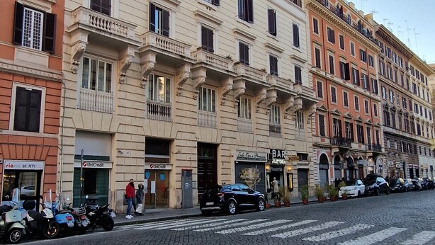 Un edificio de varios pisos con bar y restaurante en la planta baja, una calle adoquinada y vehículos estacionados.