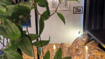 A cozy room with a bed featuring floral-patterned bedding, a wall-mounted picture, and a lit candle on a table.