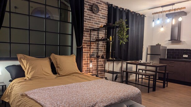 A modern bedroom with a large bed, a small table, and a kitchenette in the corner.