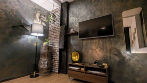 A modern living room with a brick wall, a flat-screen TV, a wooden floor, a vintage record player, and a hanging plant.