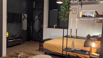 A modern bedroom with a bed, bedside table, and a dining area with plates and cutlery.