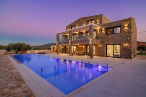 Une maison moderne à deux étages, dotée d’une piscine, d’une façade en pierre et d’un espace extérieur aménagé pour se détendre.