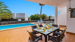 Ein Essbereich am Pool mit einem Tisch für zwei Personen, umgeben von Liegestühlen und freiem Blick auf den Pool.
