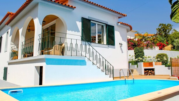A two-story house with a swimming pool, featuring a balcony with a railing, a staircase, and a garden with various plants and flowers. - Villa Casa Amelia by Villa Plus (Canico)