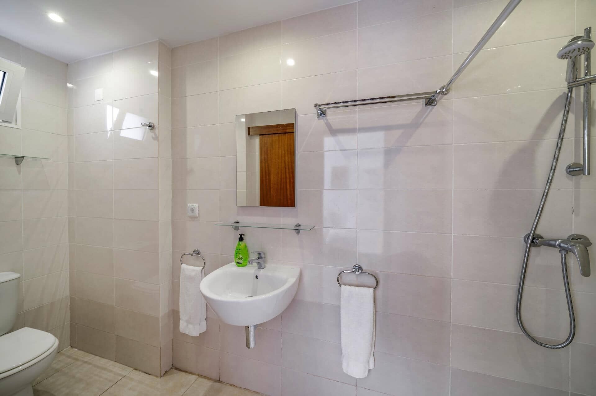 A bathroom with a toilet, sink, mirror, towel rack, and shower.