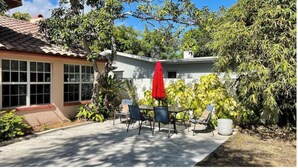 A patio with a table and chairs, surrounded by greenery and a house with a tiled roof. - Pet & Large Boat OK 1 Bed Studio Near Marina & Beach Private Lot  Sleeps 2 (Fort Pierce)