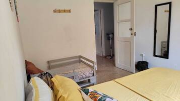 Un dormitorio con una cama, una cama individual, un armario, un espejo y una puerta que da a otra habitación.