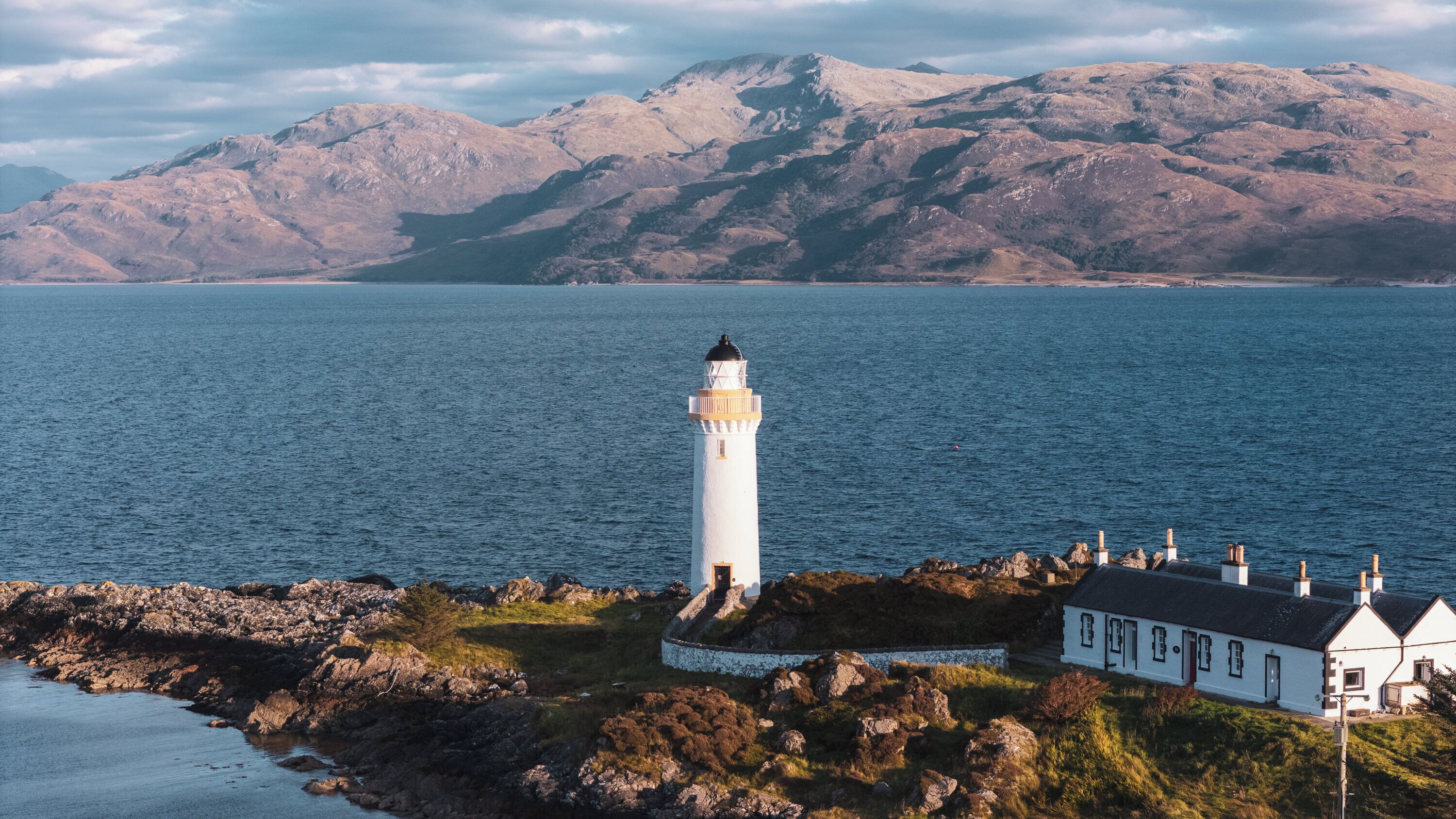 A lighthouse on a rocky coastline with a white building nearby.