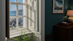 Een kamer met een groot raam met uitzicht op rotsachtig terrein en de zee.