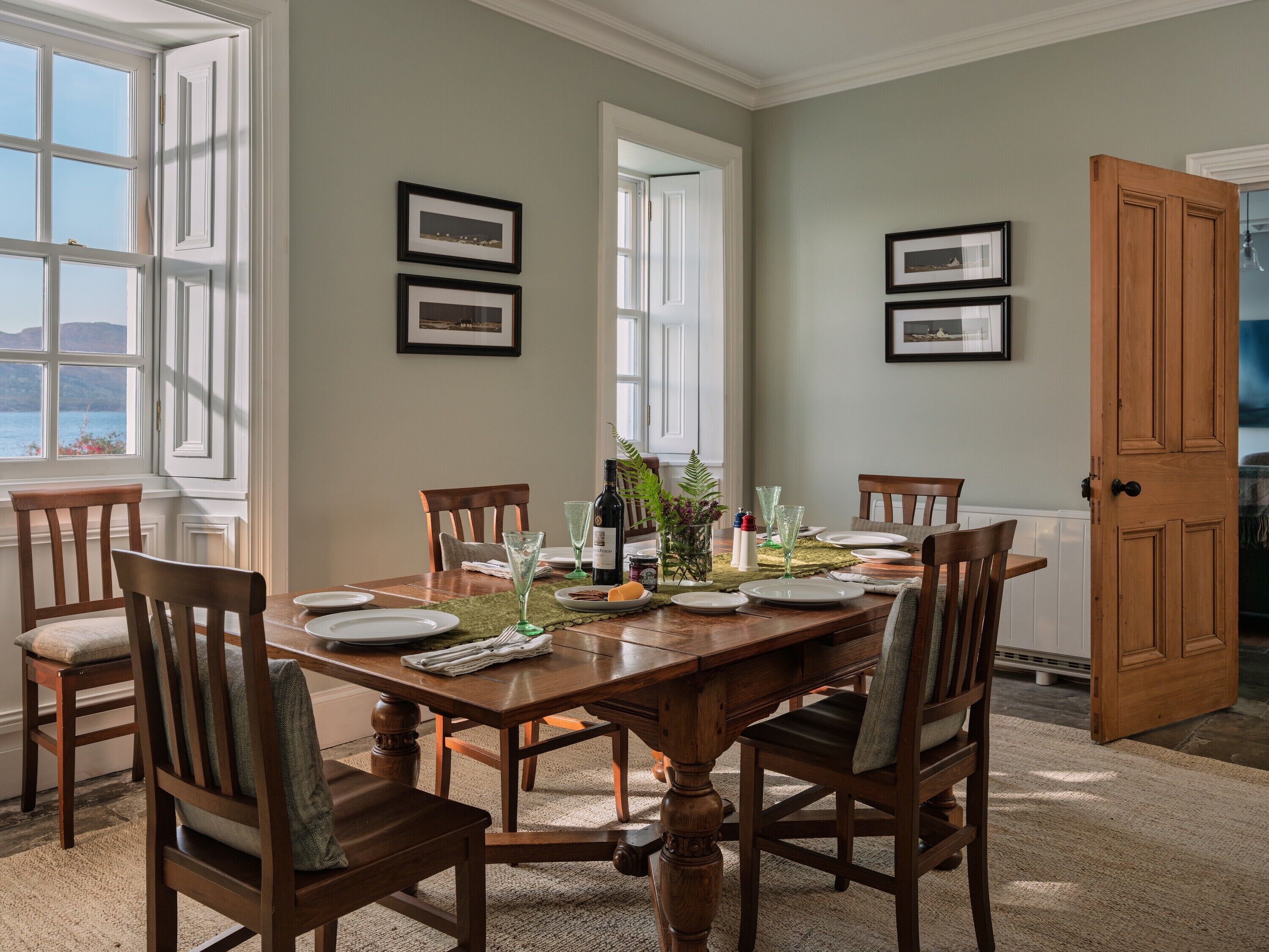 A dining room with a wooden table set for six, surrounded by chairs.