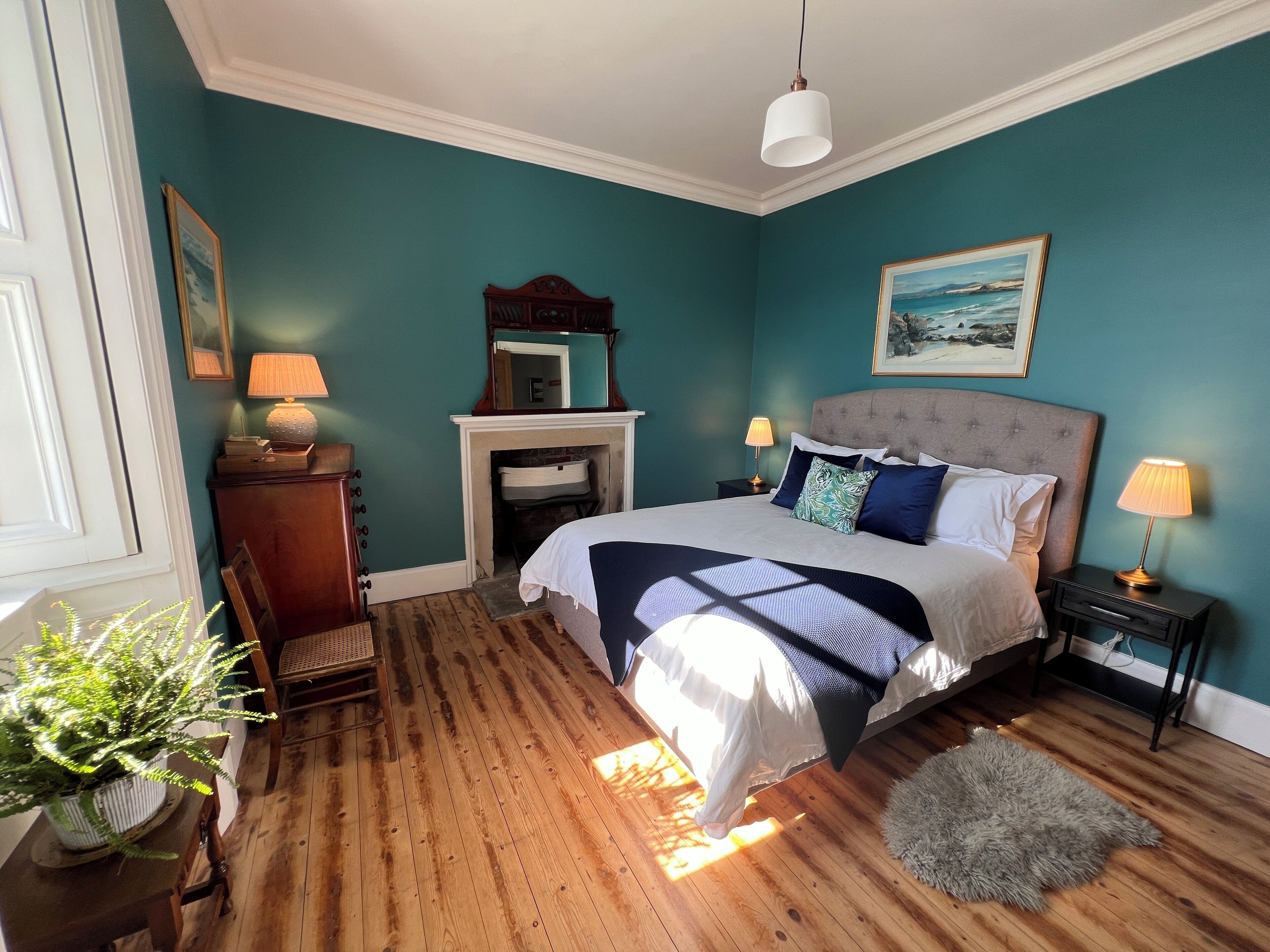 A bedroom with a bed, bedside tables, a mirror, a fireplace, and a potted plant.