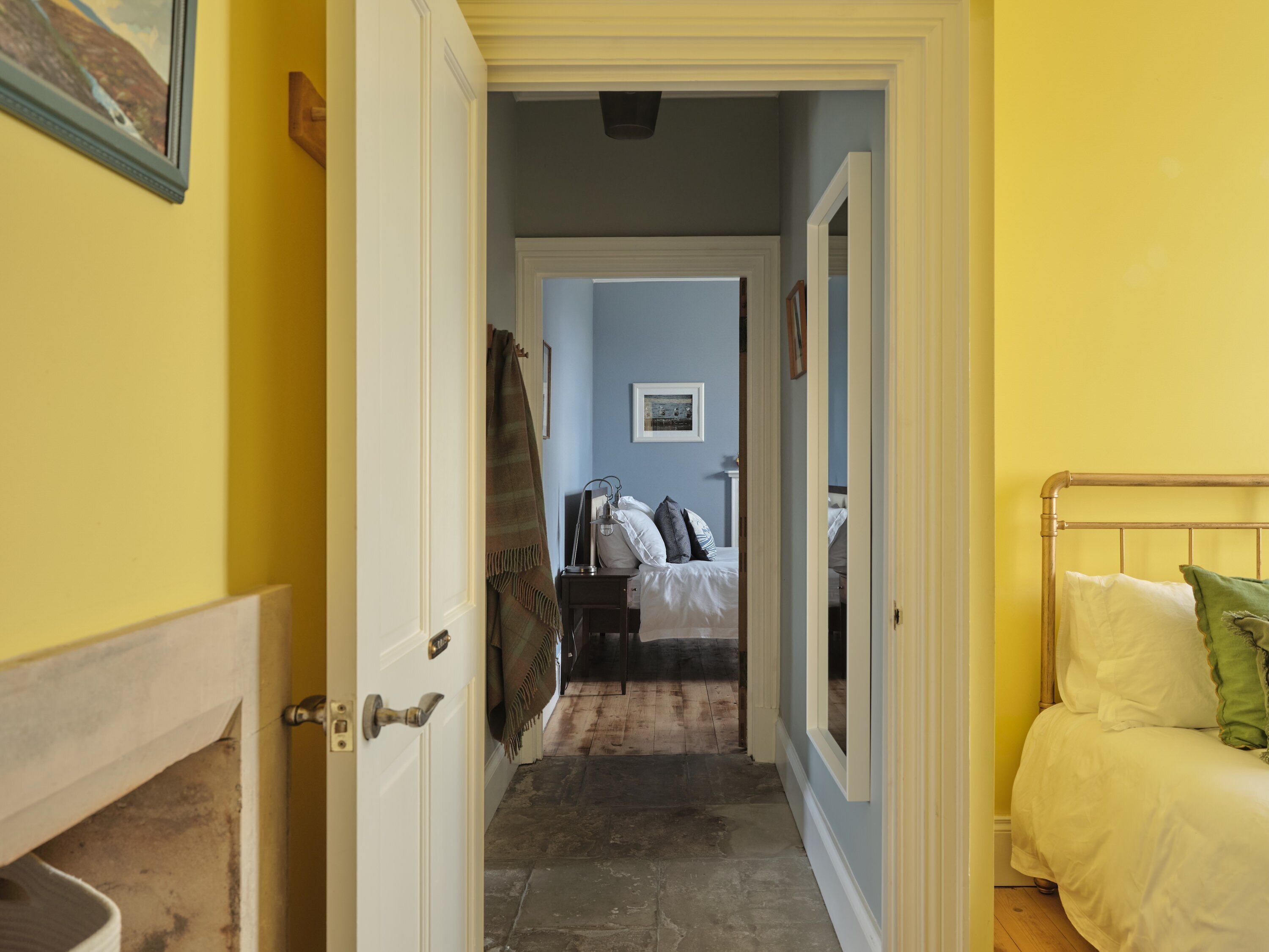 A narrow hallway leading to a bedroom with a bed, a bedside table, and a mirror.