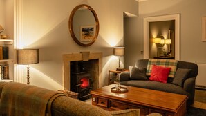 Een gezellige woonkamer met een open haard, een bank, een salontafel en een lamp.