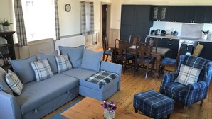 Ein Wohnzimmer mit einer Couch, Hocker und Sesseln, einem Couchtisch aus Holz sowie einem Essbereich mit Tisch und Stühlen.