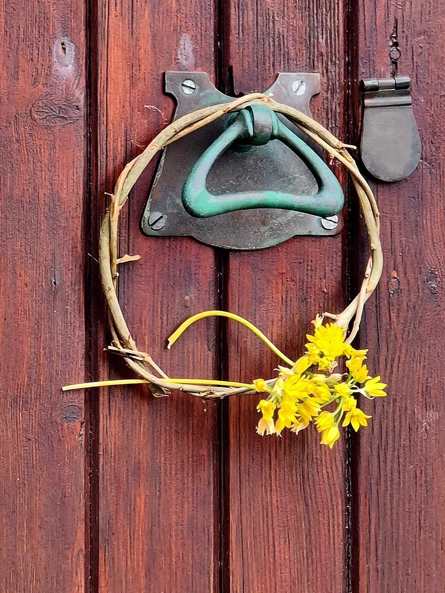 A rustic door with a metal handle and a decorative wreath with yellow flowers.