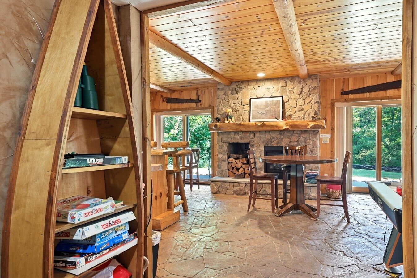 A wooden interior with a stone fireplace, a dining area, and a bookshelf filled with board games.
