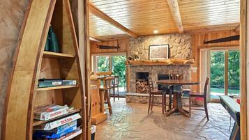 A wooden interior with a stone fireplace, a dining area, and a bookshelf filled with board games.