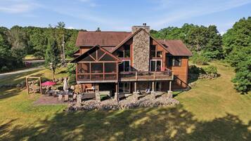 A two-story wooden house with a stone chimney, a covered deck, and a stone wall surrounding the property.
