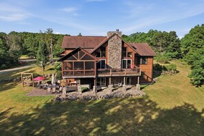 A two-story wooden house with a stone chimney, a covered deck, and a stone wall surrounding the property. - The Cabin at The Land of the Yellow River (Necedah)