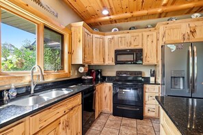 A kitchen with wooden cabinets, a stainless steel refrigerator, a microwave, a stove, and a sink. - The Cabin at The Land of the Yellow River (Necedah)